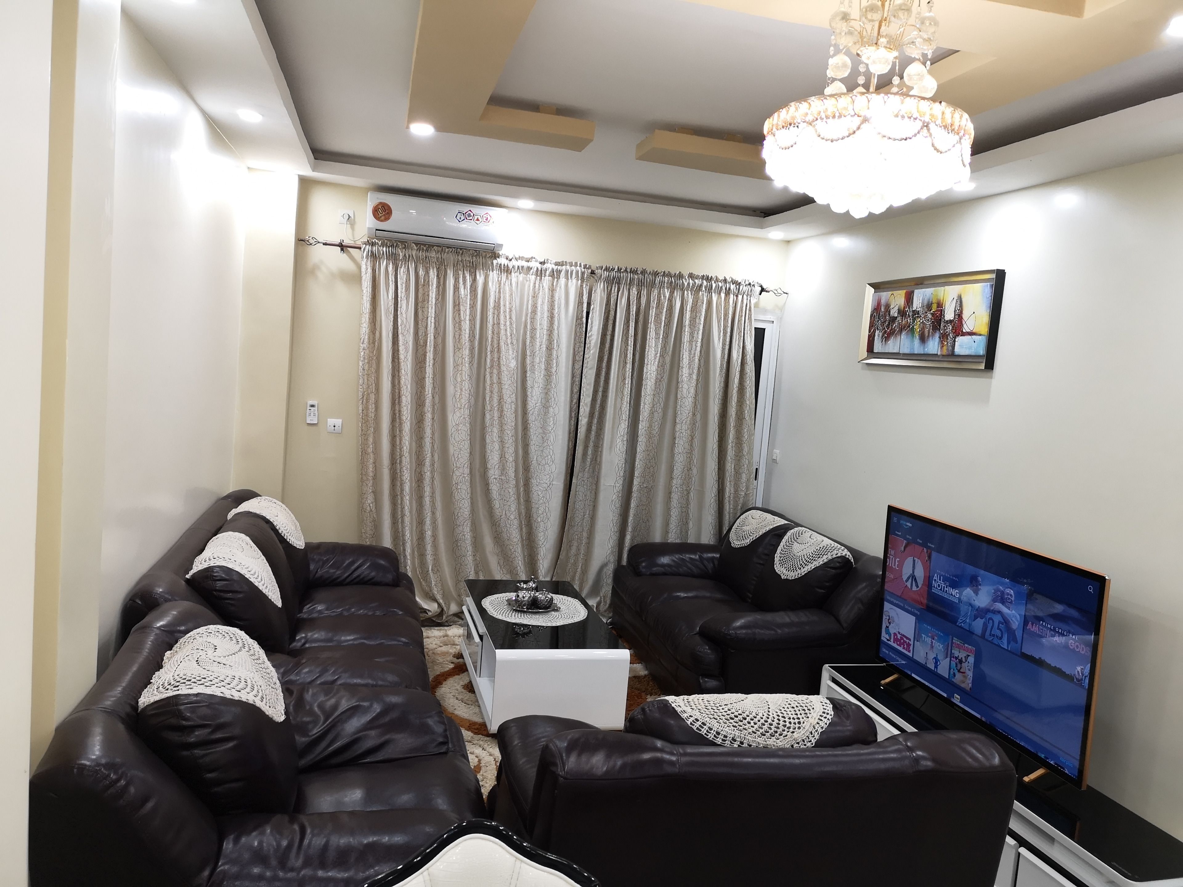 Una sala de estar con un sofá modular, una mesa de centro, un televisor y una araña.