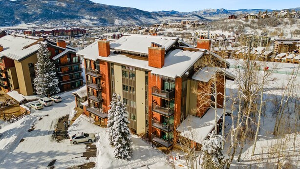 A multi-story hotel with a snow-covered roof, surrounded by a parking area and a mountainous backdrop. - Bear Claw 100 On Mountain Studio With Ski-In/Ski-Out Access! (Steamboat Springs)