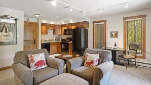 A modern kitchen with wooden cabinets, a black refrigerator, and a dining area with a table and chairs. - Bear Claw 100 On Mountain Studio With Ski-In/Ski-Out Access! (Steamboat Springs)