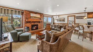 A living room with a fireplace, a sofa, a TV, and a dining area. - Bear Claw 413 Premium On Mountain Condo With Ski-In/Ski-Out Access! (Steamboat Springs)