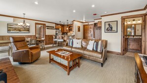 A spacious living room with a leather recliner, a sofa, and a coffee table. There is a dining area with wooden furniture and a kitchen visible through an open door. - Bear Claw 413 Premium On Mountain Condo With Ski-In/Ski-Out Access! (Steamboat Springs)