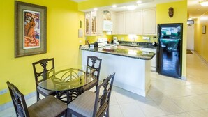 A compact kitchen with white cabinets, a central island, and a dining area with a glass table and chairs.