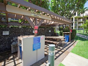 A covered outdoor area with a grill sign, picnic tables, a barbecue area sign, and a stone wall. - Suite Living w/Island Touches! Updated Kitchen, Lanai, WiFi–Kamaole Sands 1206 (KIHEI)