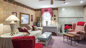 A living room with a sofa, armchair, and ottoman, a table with a lamp, and a fireplace with a red blanket.