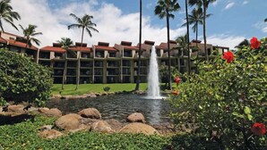A hotel with a pool, palm trees, and a waterfall.