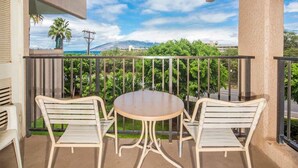 A balcony with two white metal chairs and a round table, overlooking a green landscape with trees and a mountain in the distance.