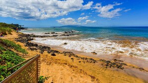 A beach with a wooden fence, rocky shoreline, and clear blue sky.