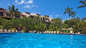 A hotel pool with clear blue water, surrounded by palm trees and lounge chairs.