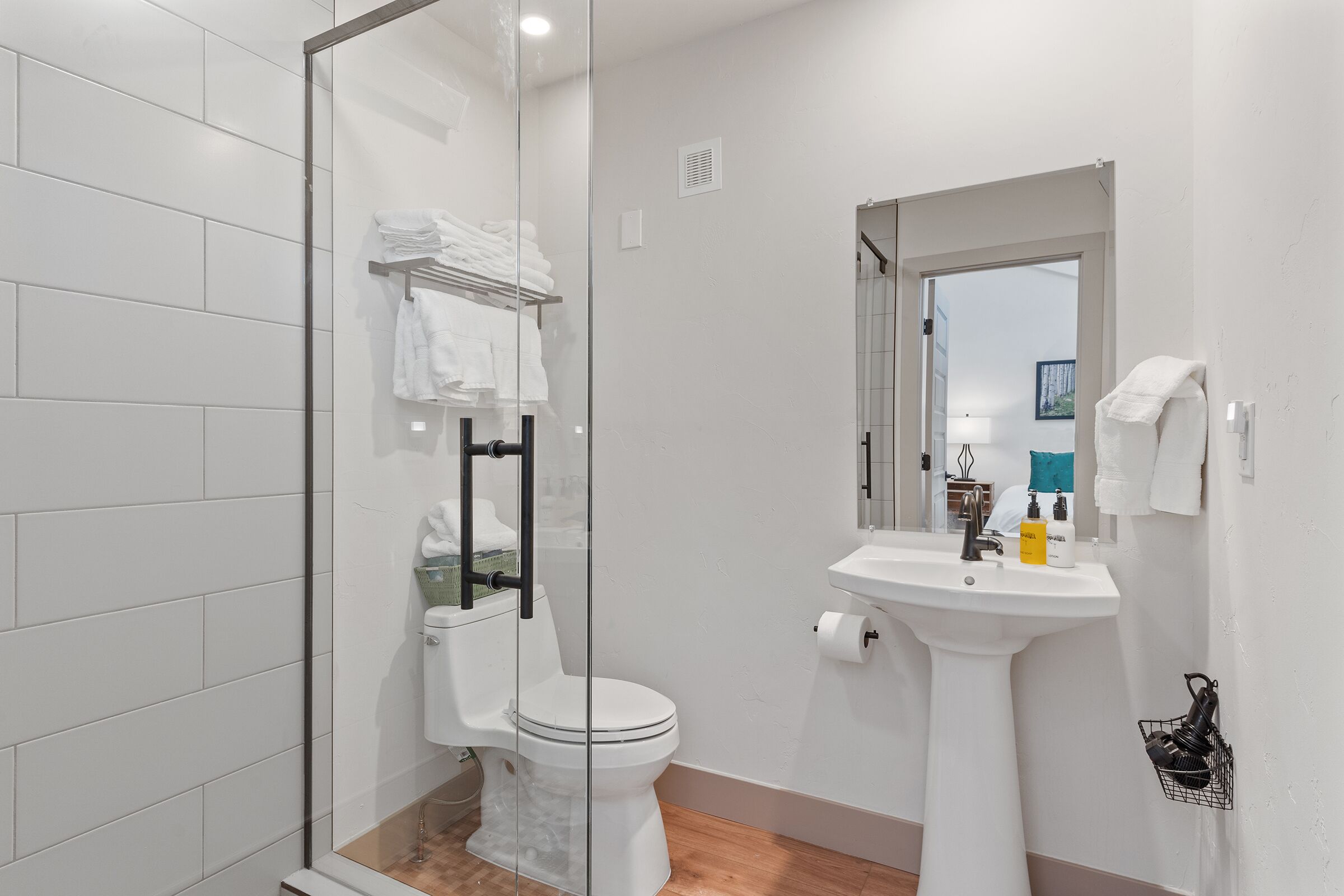 Une salle de bain moderne avec une douche à parois de verre, des toilettes blanches, un lavabo avec des articles de toilette et un porte-serviettes.