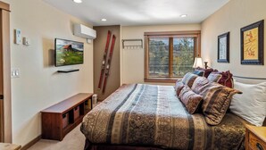 Ein Schlafzimmer mit einem großen Bett, einem Fernseher, einem Skiständer und einem Fenster mit Jalousien.