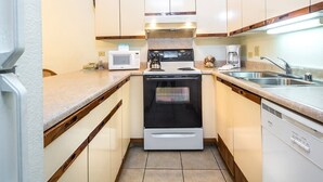 Una cocina compacta con armarios blancos, horno empotrado, microondas y un lavamanos.