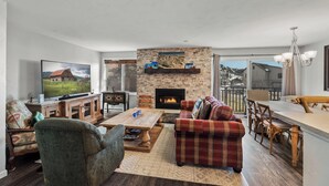 A cozy living room with a fireplace, a television, and a dining area with a wooden table and chairs. - Bear Claw 109 on Mountain Condo with Ski-In/Ski-Out Access! (Steamboat Springs)