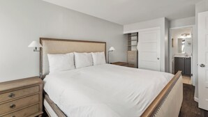 A neatly arranged bedroom with a large bed, bedside tables, a wardrobe, and a bathroom visible in the background. - Bear Claw 109 on Mountain Condo with Ski-In/Ski-Out Access! (Steamboat Springs)