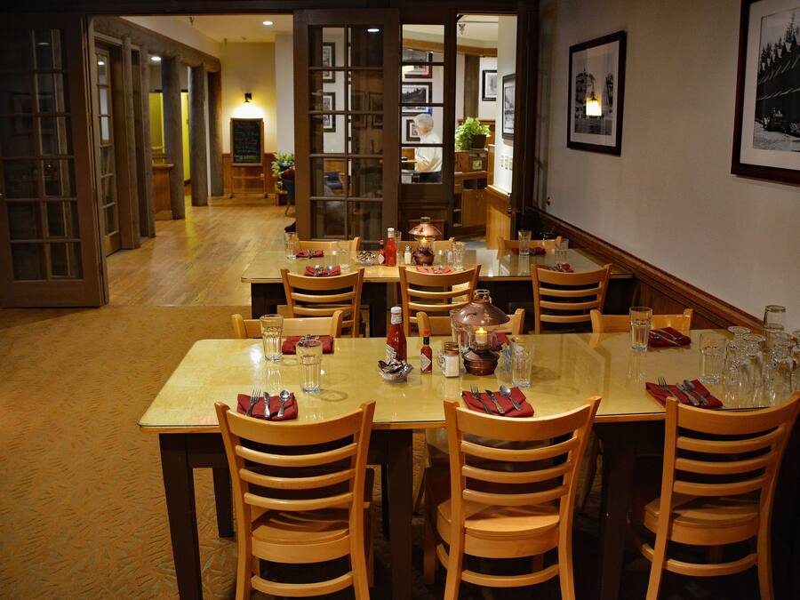 A restaurant with multiple tables and chairs, a wooden floor, and framed pictures on the walls.