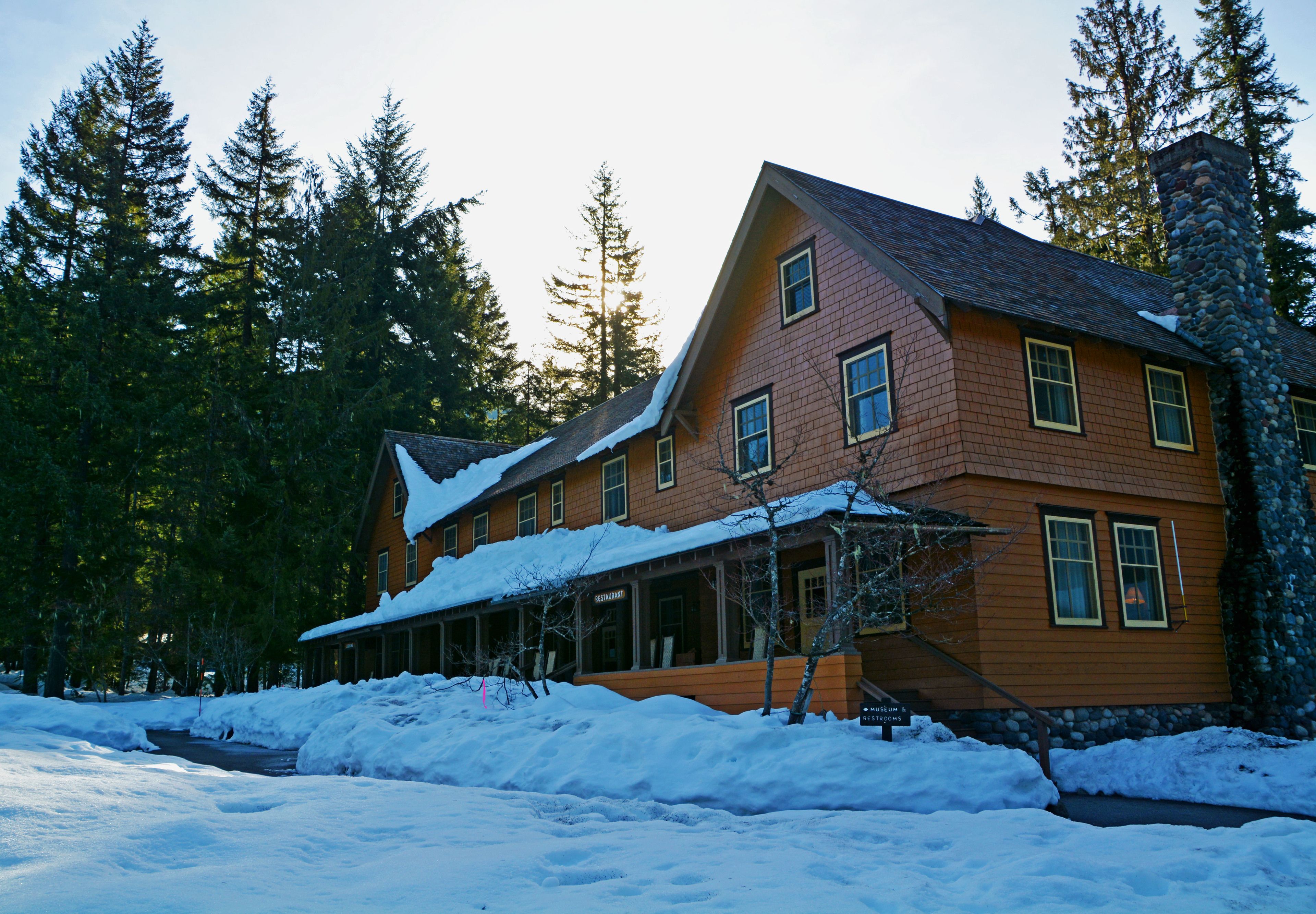 Un grand bâtiment en bois à plusieurs étages, avec un toit enneigé et une cheminée en pierre.