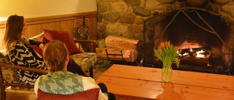 Un salón acogedor con chimenea de piedra, muebles de madera y un jarrón de flores sobre una mesa.
