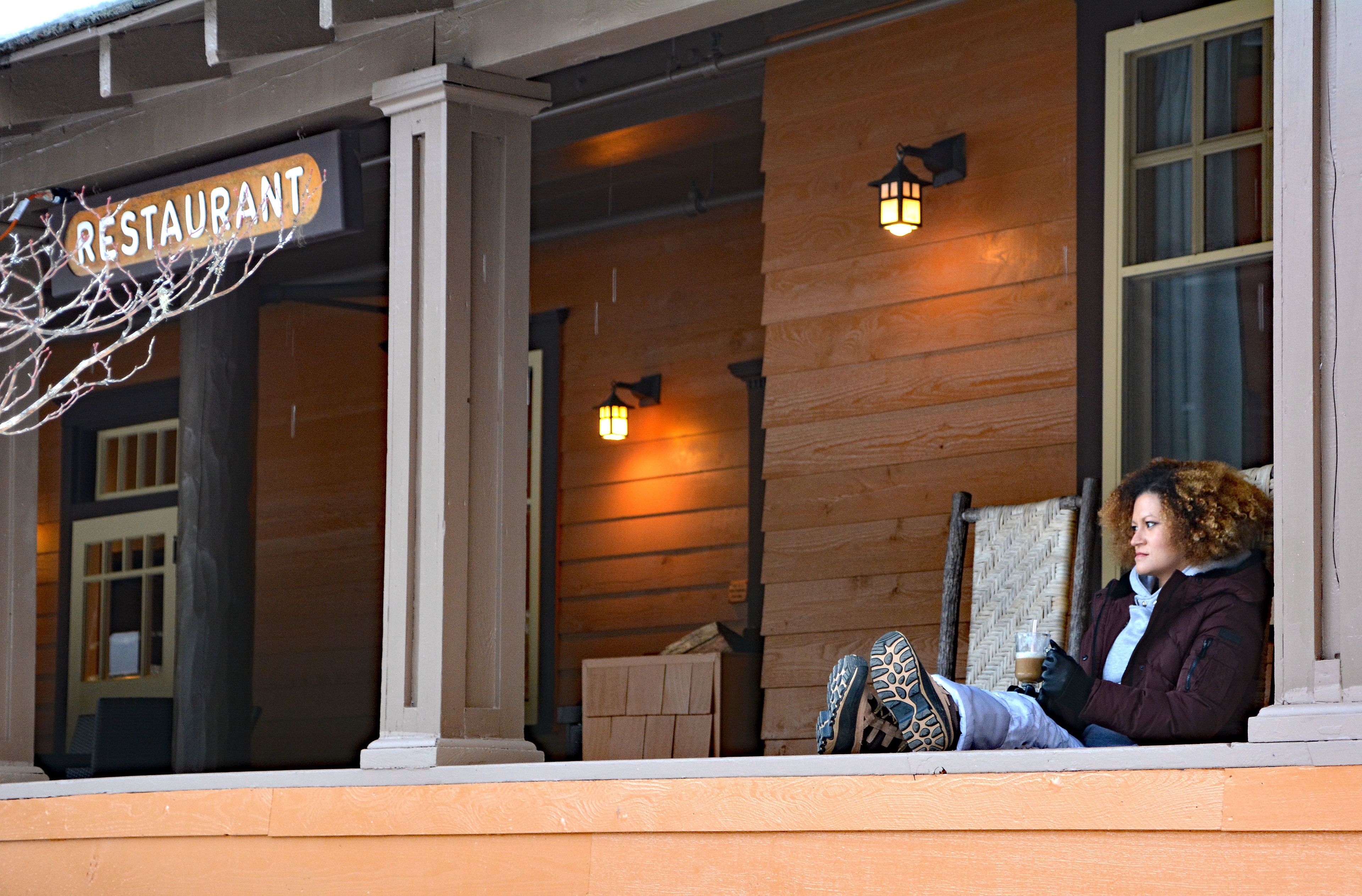 A person sitting on a porch with a sign that reads "RESTAURANT" above.