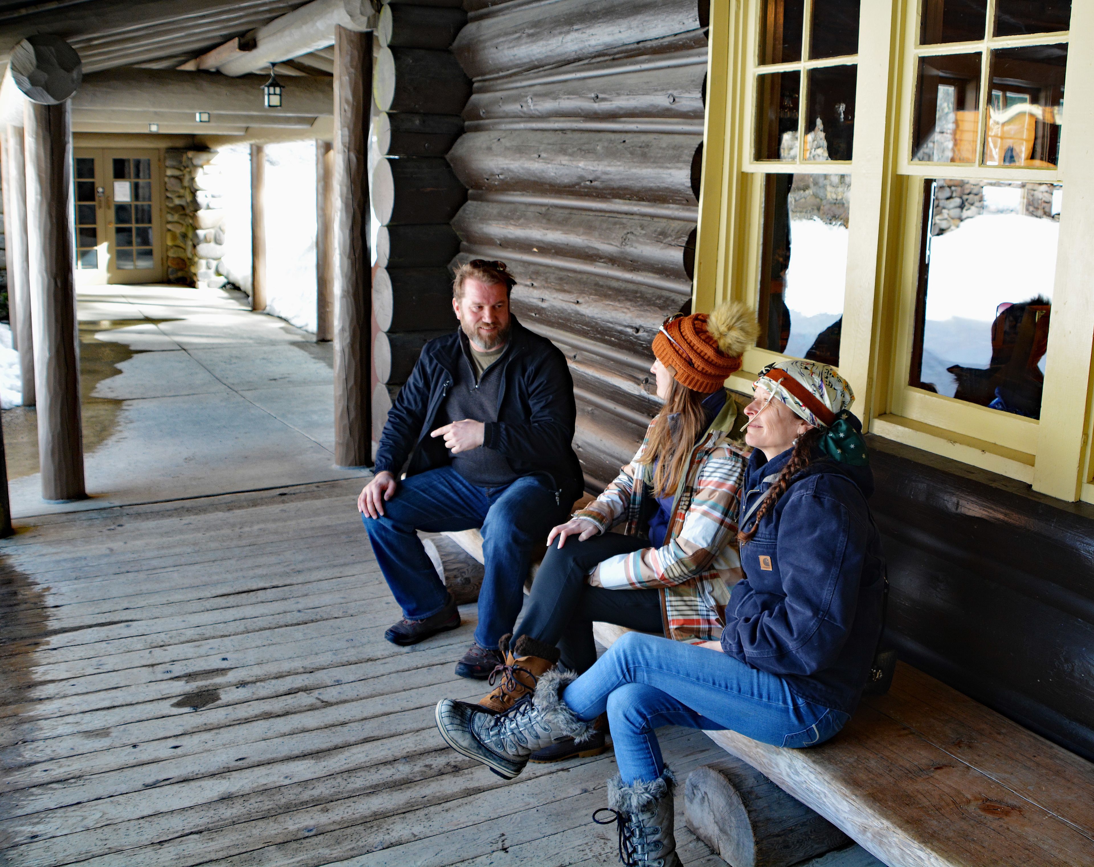 A wooden cabin with a porch where three people are seated.