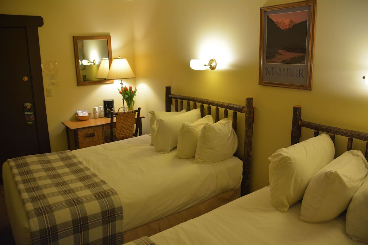 Ett hotellrum med två sängar, en sänggavel i trä, ett nattduksbord med en lampa, en inramad tavla på väggen och en receptionsdisk.