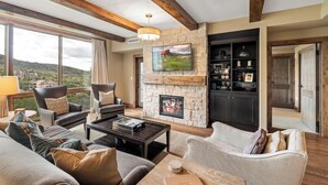 Amplia sala de estar con chimenea de piedra, asientos cómodos, televisor y vistas al exterior.