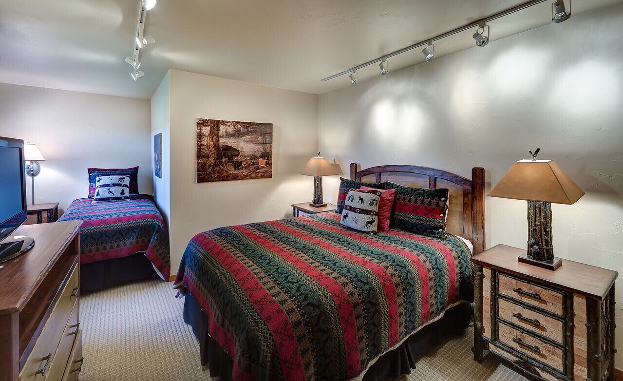 A bedroom with two beds, a desk, a lamp, and a painting on the wall.