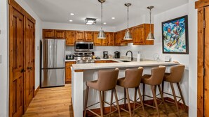 Une cuisine moderne avec des meubles en bois, des appareils électroménagers en acier inoxydable et un coin bar avec des tabourets.
