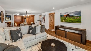 Un salon moderne avec un canapé d’angle, une table basse et un tableau représentant un paysage rural.