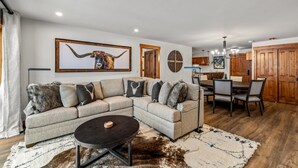 Un salon moderne avec un canapé d’angle, une table basse ronde et un coin repas comprenant une table et des chaises en bois.