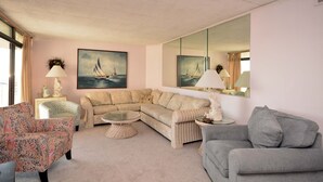 A living room with a beige sectional sofa, a patterned armchair, a round coffee table, and a large mirror.
