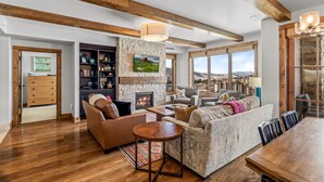 A spacious living room with a fireplace, wooden beams, and a large window overlooking a cityscape.
