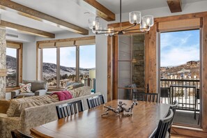 A dining area with a wooden table and chairs, a chandelier, and large windows offering a mountain view. - Edgemont 2401 Luxury On Mountain Condo With Ski-In/Ski-Out Access! (Steamboat Springs)