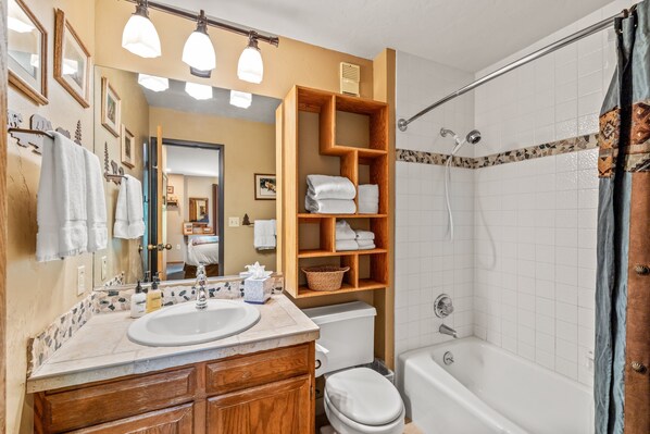 A bathroom with a sink, mirror, wooden shelves with towels, a toilet, and a bathtub.
