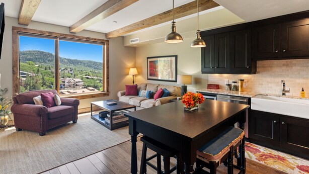 A modern kitchen with dark cabinets, a large island, and a view of a green landscape. - Edgemont 2504 Luxury On Mountain Condo With Ski-In/Ski-Out Access! (Steamboat Springs)