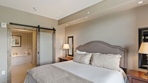 A neatly arranged bedroom with a large bed, a bedside table with a lamp, and a bathroom visible through an open door. - Edgemont 2504 Luxury On Mountain Condo With Ski-In/Ski-Out Access! (Steamboat Springs)