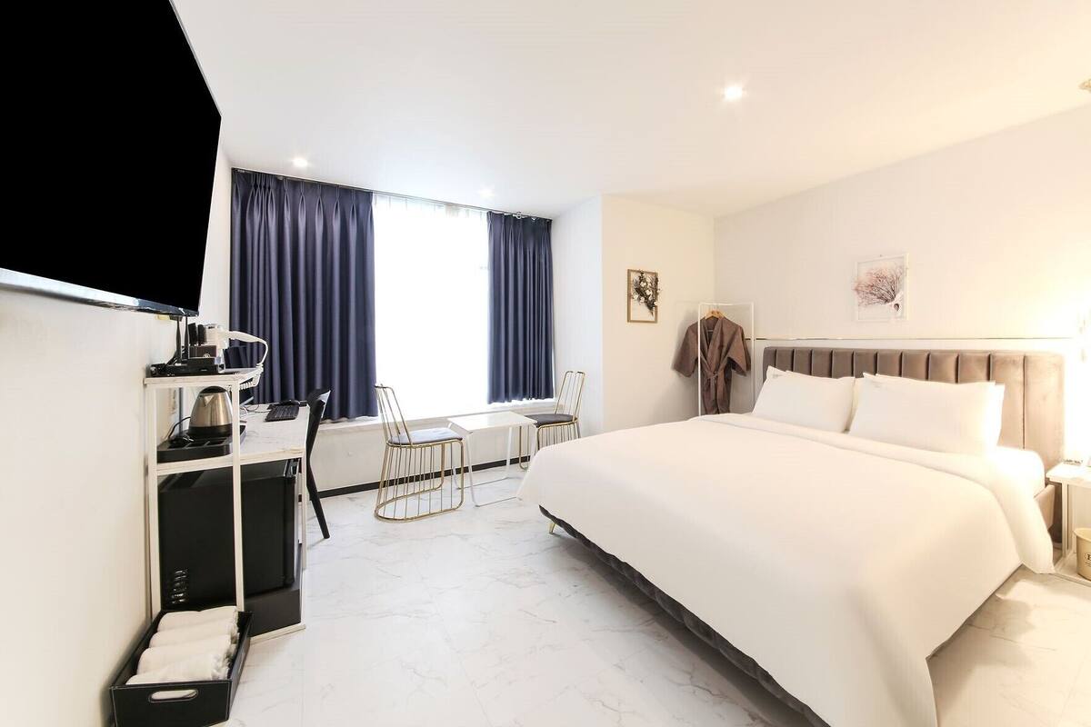 Une chambre d’hôtel avec un lit, un bureau et une chaise, une télévision et une fenêtre avec des rideaux.
