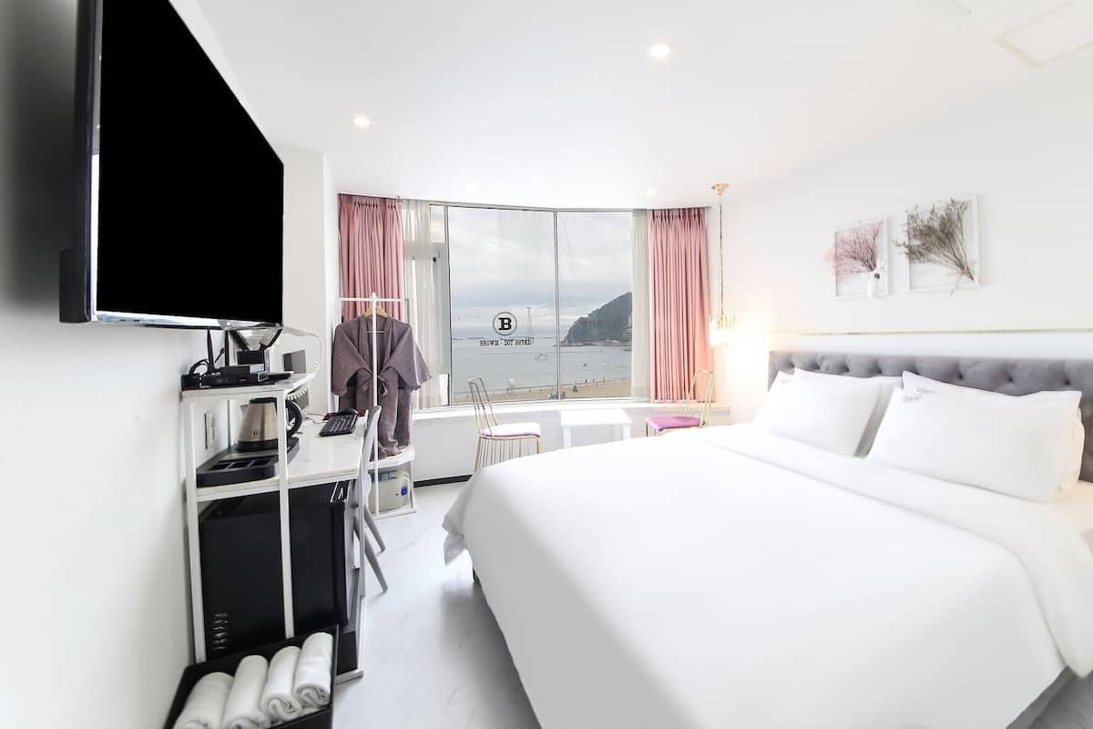 Une chambre d’hôtel avec un lit, un bureau équipé d’un ordinateur, une télévision et une vue sur la mer.
