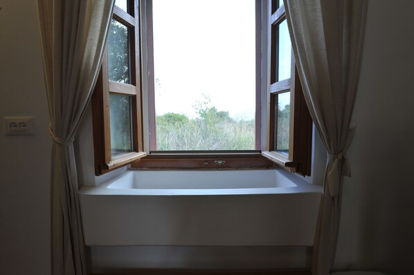 A bathroom with a window, a sink, and a power outlet on the wall.