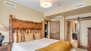 Une chambre avec un grand lit, une tête de lit en bois et une porte coulissante donnant accès à une salle de bain.