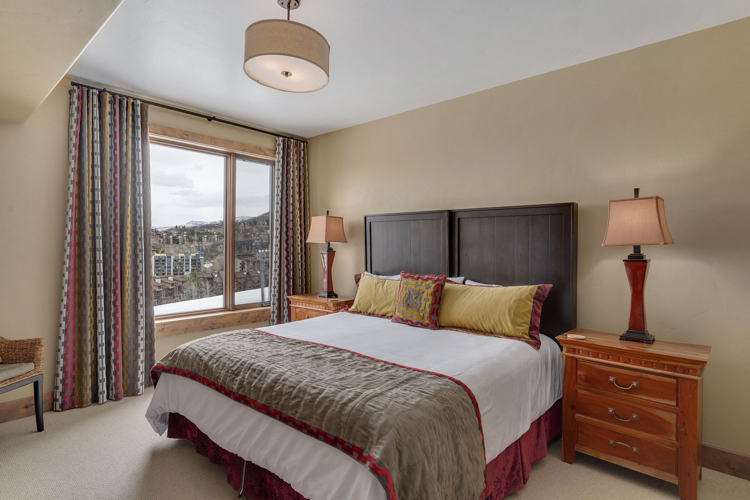Une chambre d’hôtel avec un grand lit, deux tables de chevet avec des lampes, une vue sur le paysage urbain par la fenêtre et un luminaire au plafond.