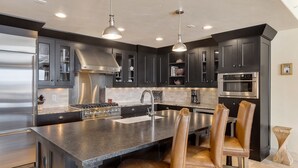 Une cuisine moderne avec des meubles de couleur sombre, des appareils en acier inoxydable et un îlot central doté de tabourets de bar.