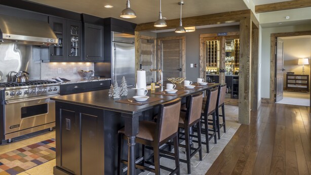 Una cocina moderna con electrodomésticos de acero inoxidable, una isla central con taburetes de bar y un techo de madera.