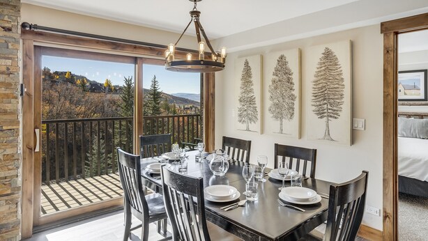 A dining area with a table set for six, large windows, and a view of a mountainous landscape. - Bear Claw 302 Premium On Mountain Condo With Ski-In/Ski-Out Access! (Steamboat Springs)