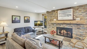 A modern living room with a stone fireplace, comfortable seating, and artwork on the walls. - Bear Claw 302 Premium On Mountain Condo With Ski-In/Ski-Out Access! (Steamboat Springs)