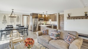 A modern kitchen with stainless steel appliances, a dining area with a wooden table and chairs, and a living room with a sofa and decorative pillows. - Bear Claw 302 Premium On Mountain Condo With Ski-In/Ski-Out Access! (Steamboat Springs)