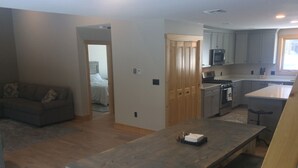 A modern kitchen with a central island, a dining area with a wooden table, and a living room with a sofa.