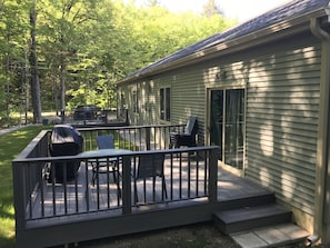 Enjoy a relaxing moment on the deck with a table and chairs, surrounded by a well-manicured lawn and lush trees.
