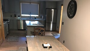 A modern kitchen with stainless steel appliances, a wooden dining table, and a patterned rug.