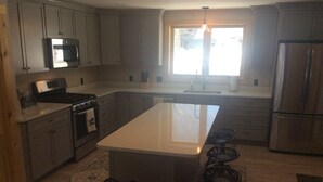 A modern kitchen with grey cabinets, a central island with bar stools, a built-in oven, and a stainless steel refrigerator.