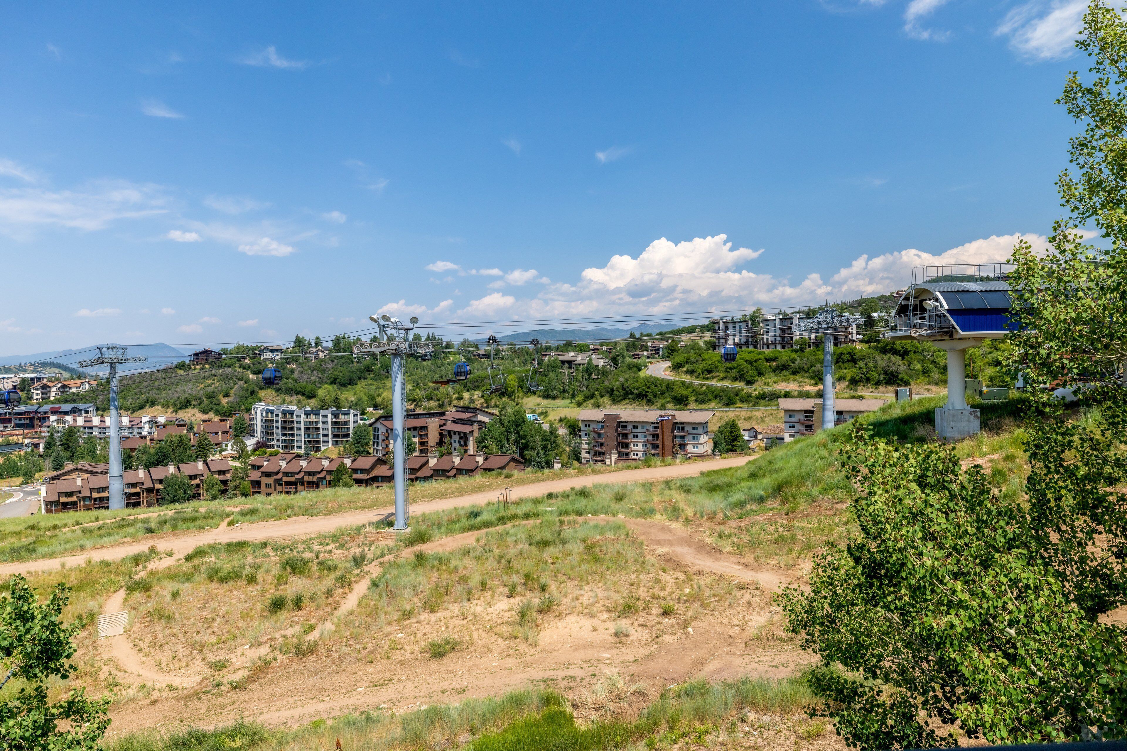 Vista lateral de uma colina mostrando uma área residencial com vários edifícios, incluindo um grande hotel com design moderno e um sistema de teleférico.