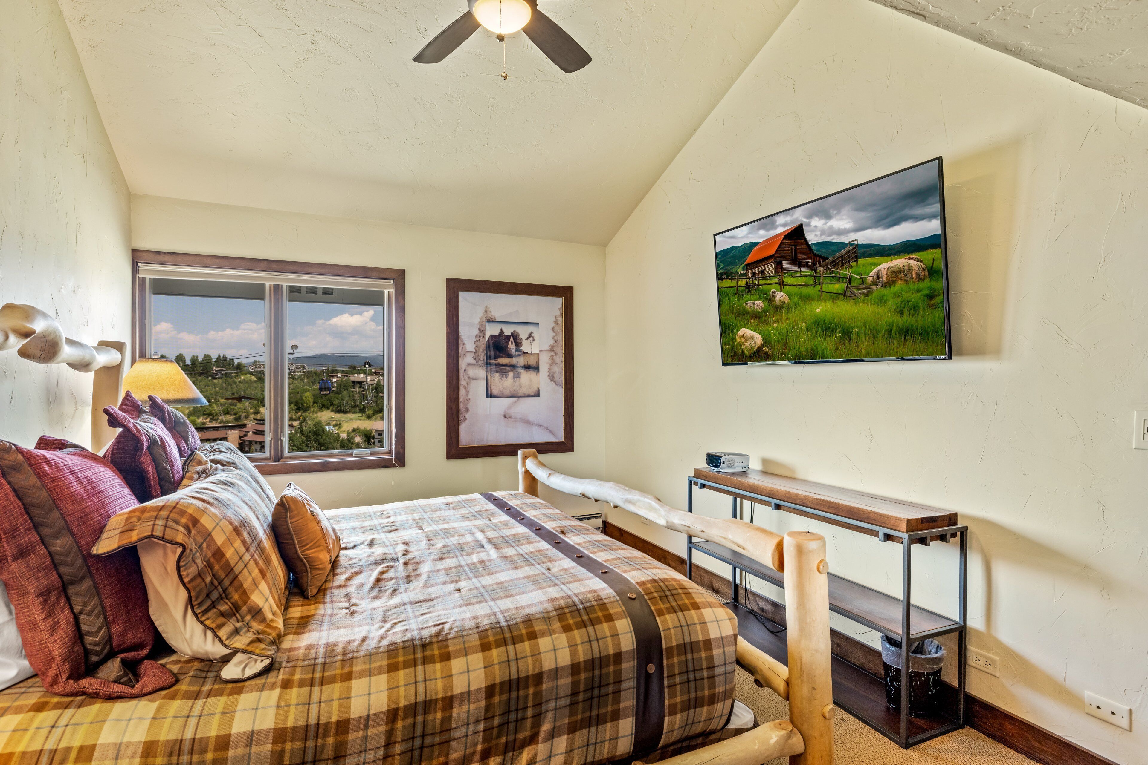 Ein Schlafzimmer mit Bett, Fenster, Fernseher und einer Holzbank.